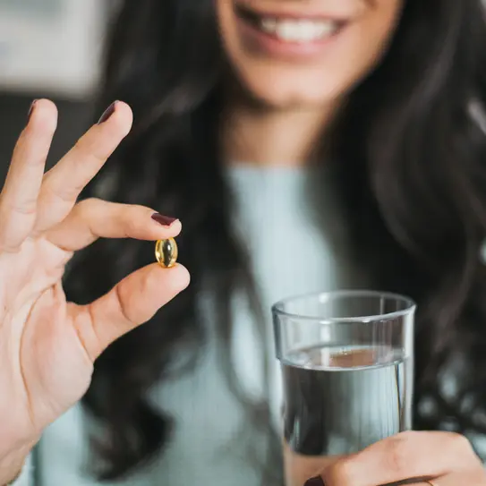 Lächelnde Frau mit einer Omega-3-Kapsel in der Hand